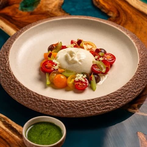 Burrata with farm tomatoes — Creamy burrata paired with sweet cherry tomatoes, grapes, and aromatic pesto sauce. Light, juicy, an