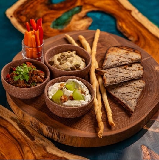 Dip selection with young veggies — A flavorful selection of homemade hummus, babaganoush, and creamy gorgonzola mousse. Served with gri