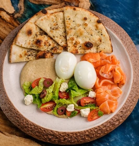 Mediterranean breakfast — A vibrant breakfast with poached eggs, salted salmon, hummus, fresh salad, feta, olives, and warm fl