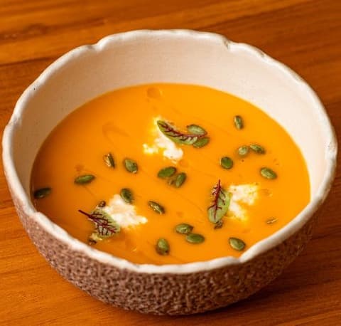 Pumpkin cream Soup — Velvety pumpkin cream soup served with stracciatella, truffle oil, and crunchy pumpkin seeds. Smooth