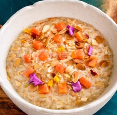Sweet oatmeal with seeds and fruit — Creamy oatmeal cooked with oat milk and served with flaxseeds, almond slices, and fresh papaya. Ligh