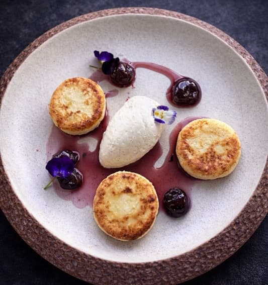 Syrniki — Soft cottage cheese pancakes served with mascarpone-banana cream and cherry compote. Delicate, cream